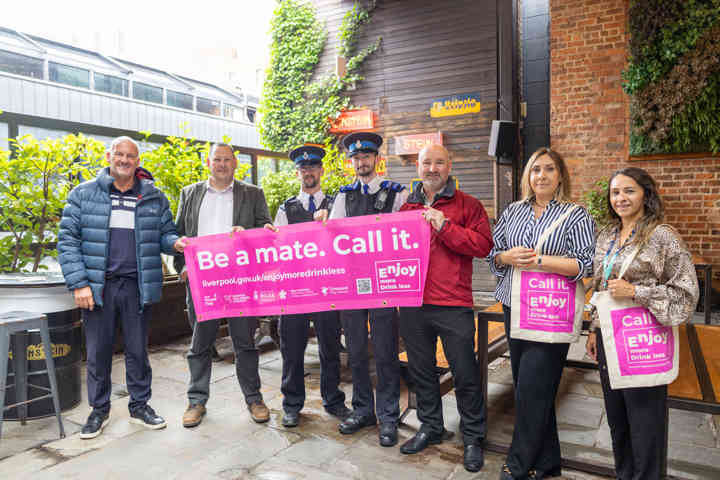 Group of people in bar holding pink sign that reads, call it, be a mate.