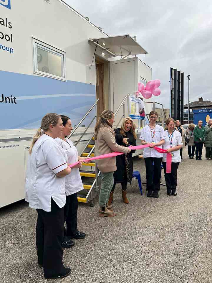 A group of healthcare staff and attendees gather outside a mobile breast screening unit for a ribbon‑cutting ceremony.