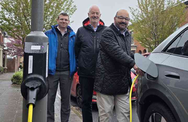 Three people posing behind am electric vehicle charger