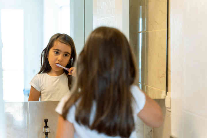 Little Girl Smiling at Herself While Brushing Teeth at Home in the Morning