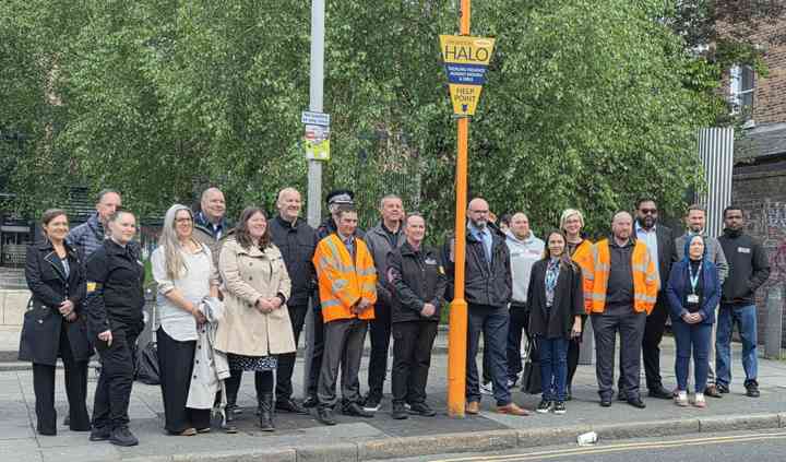 A group of people stood by an orange streetlight, with Halo Point signs on it