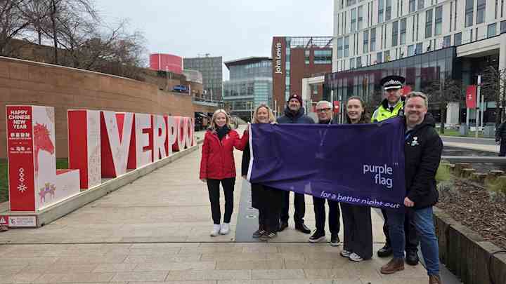 People stood by a Liverpool sign, holding a Purple Flag