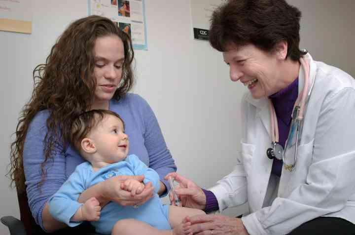 A nurse giving a baby a vaccine. Baby is smiling. Mother is holding the baby.